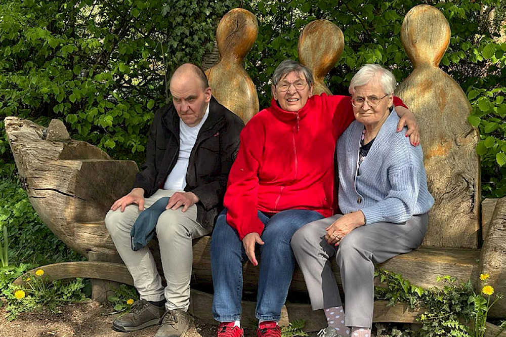 Bild zeigt drei Personen auf einer Holzbank.