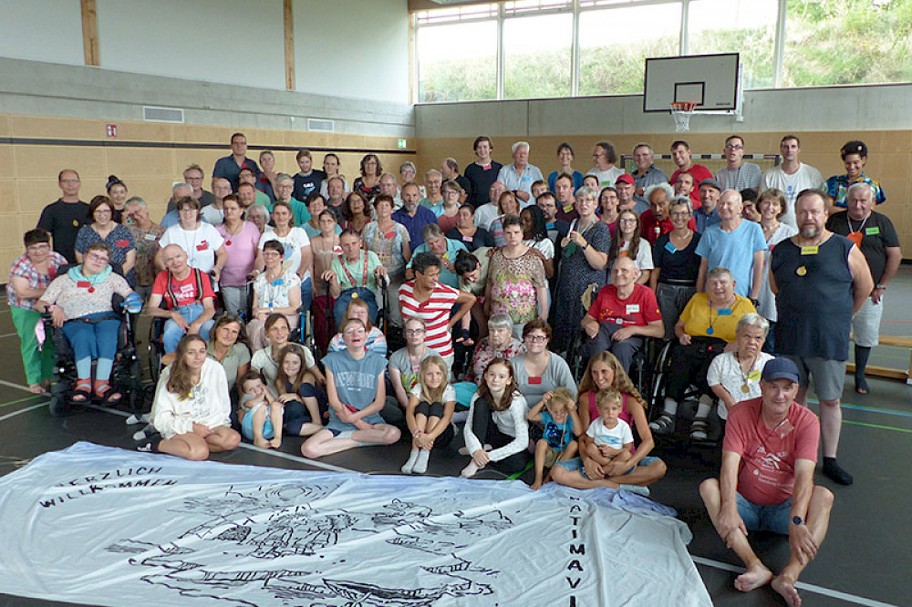 Bild zeigt eine Gruppe Menschen in einer Turnhalle mit einem großen Stoffbanner.