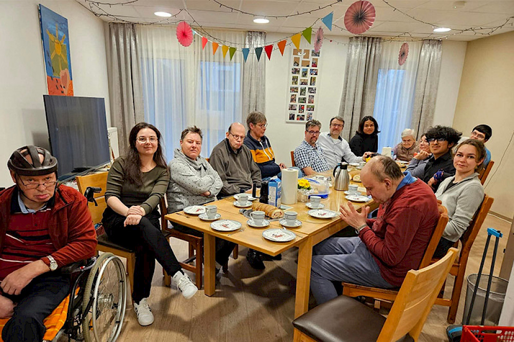 Bild zeigt viele Personen an einem Kaffeetisch.