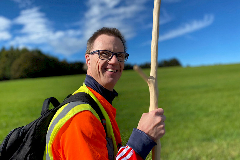 Bild zeigt eine Person in der Natur mit einem Wanderstock.